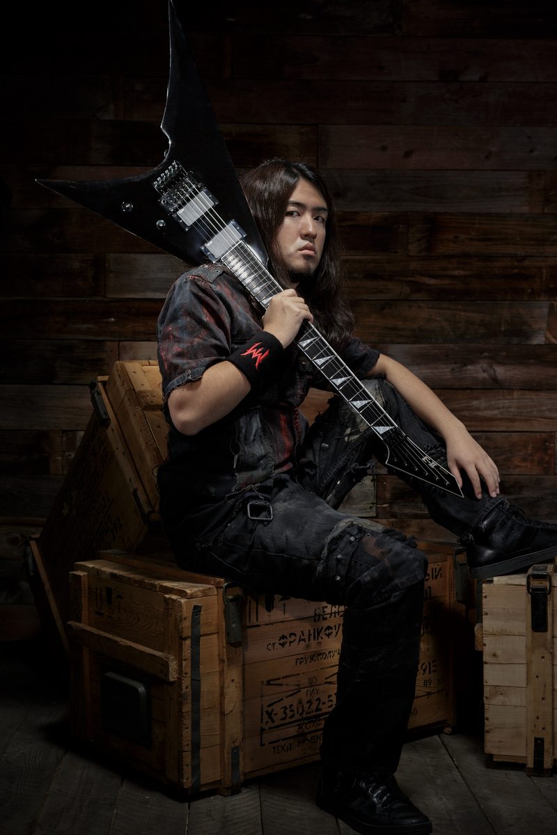Masaki Murashita seated on wooden crates, holding a black electric guitar