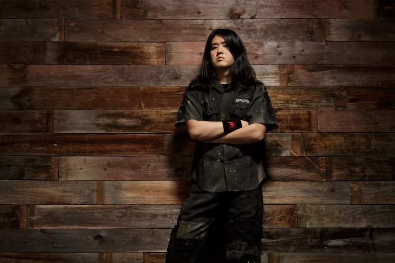Masaki Murashita standing with folded arms against a wooden wall