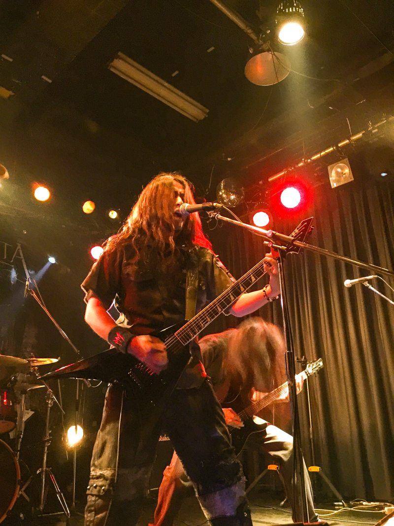 Masaki Murashita singing and playing guitar under red and amber stage lights