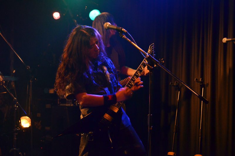 Masaki Murashita performing with a guitar at the microphone under blue stage lighting