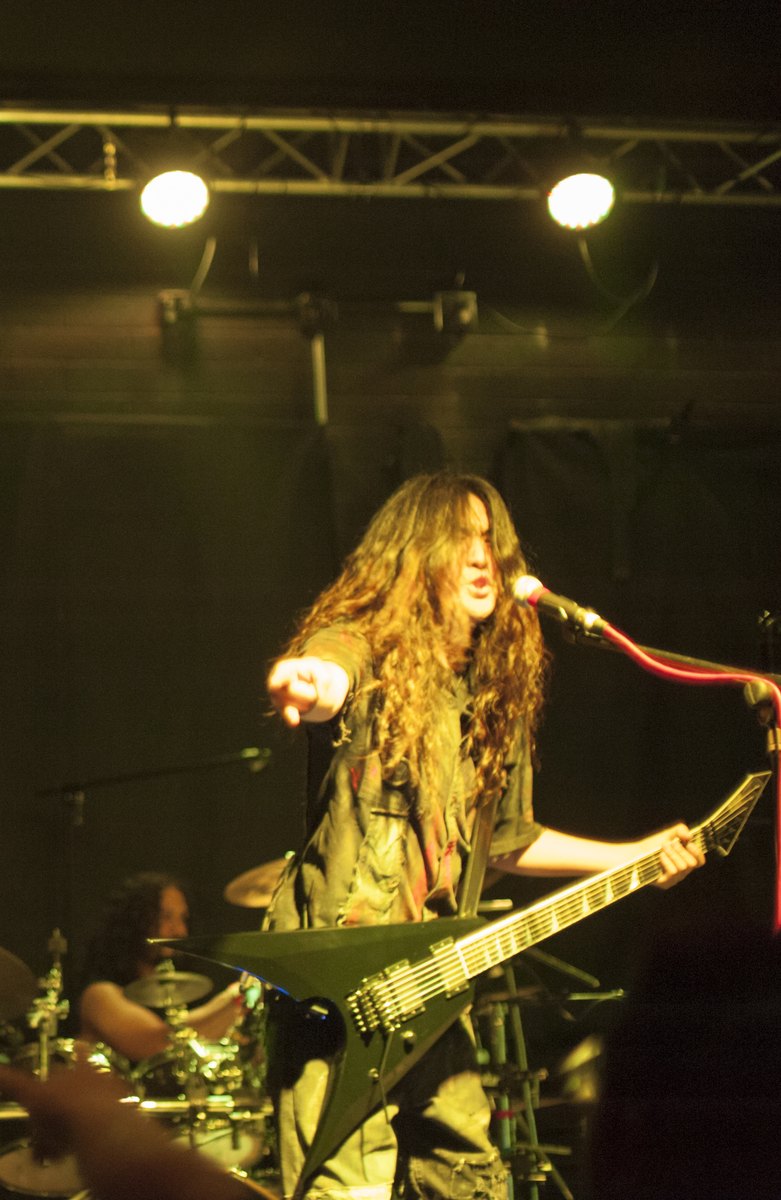 Masaki Murashita pointing toward the audience while holding his guitar under yellow stage lights