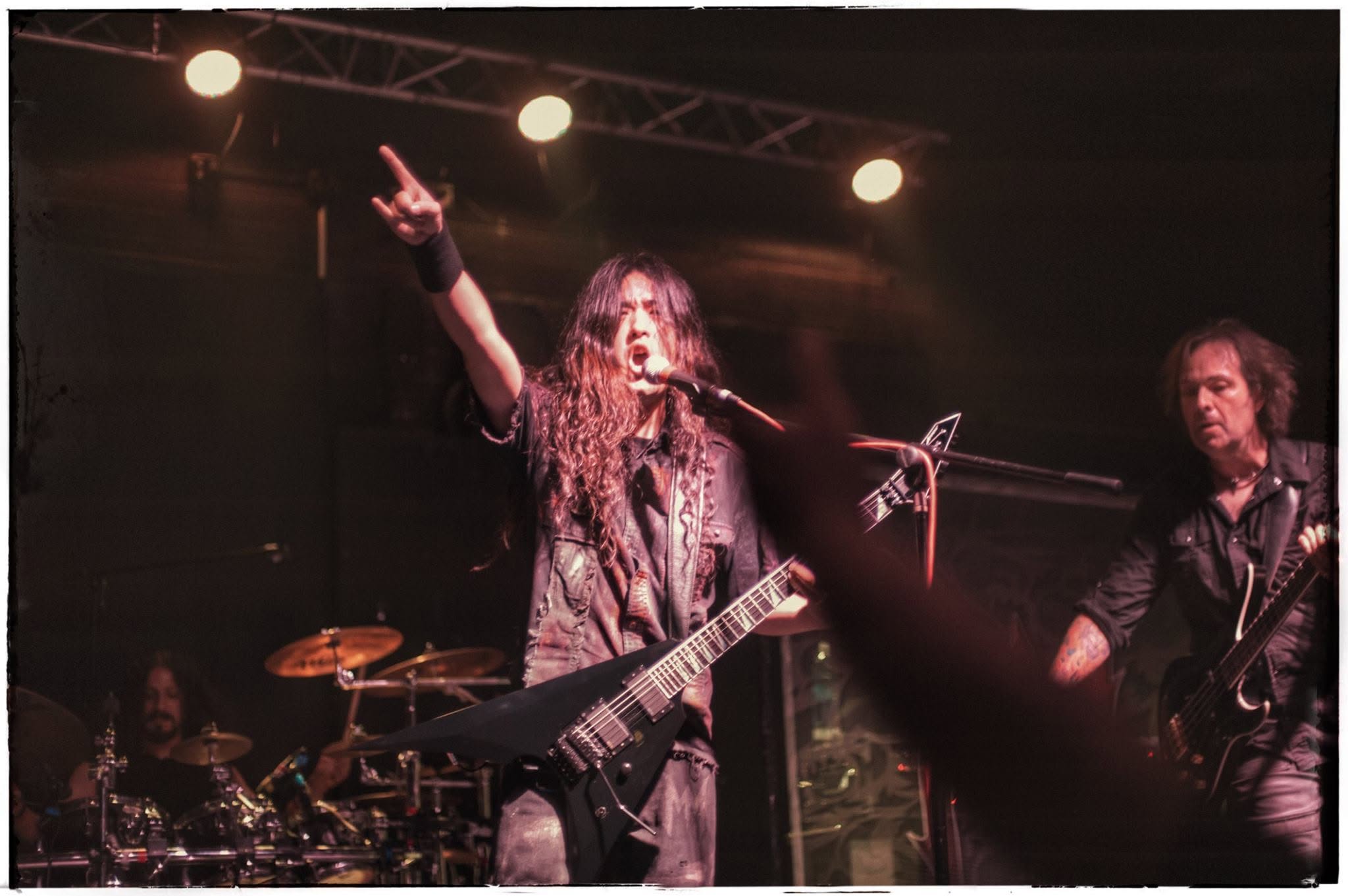 Masaki Murashita singing and playing guitar on stage with his arm raised